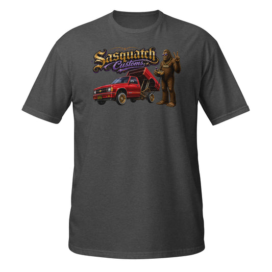 Sasquatch Customs Lowrider Series t-shirt — Bigfoot hitting the switches next to a Chevy S10 bed dancer mini truck on hydraulics — funny Sasquatch mini truck tee on black — Rod Shop Collective